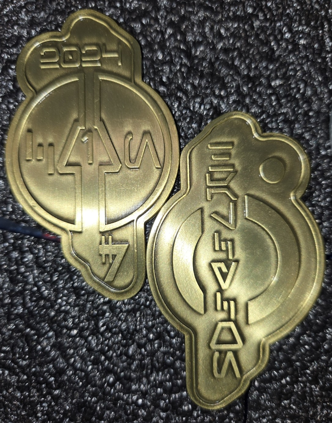 Two views of a gold-toned shaped commemorative credit dated 2024