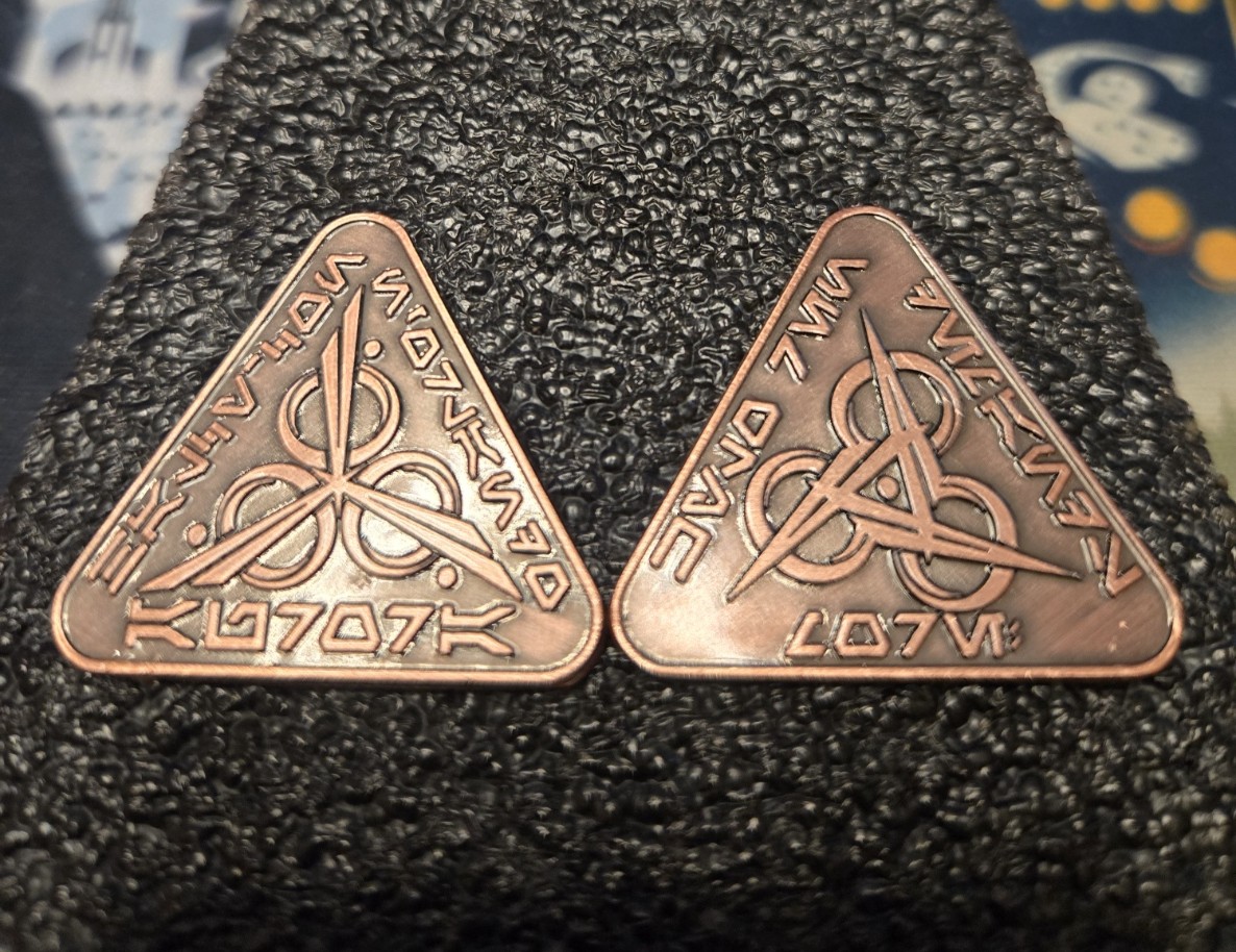 Two copper-toned triangular Aurora commemorative pieces with engraved symbols